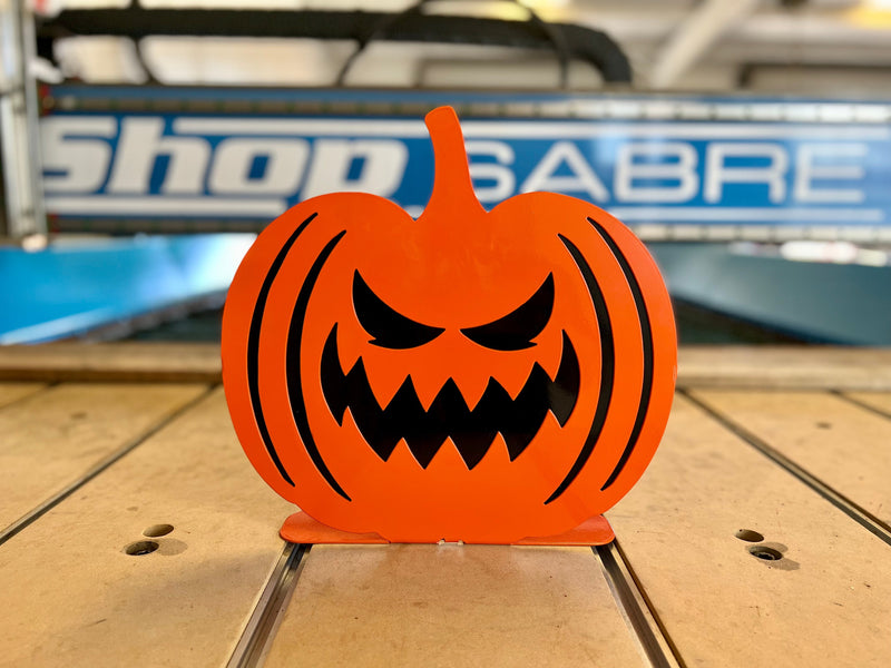 Front view of an orange steel jack-o'-lantern featuring a classic vampire-style carved face with two sharp fangs and a wide grin.